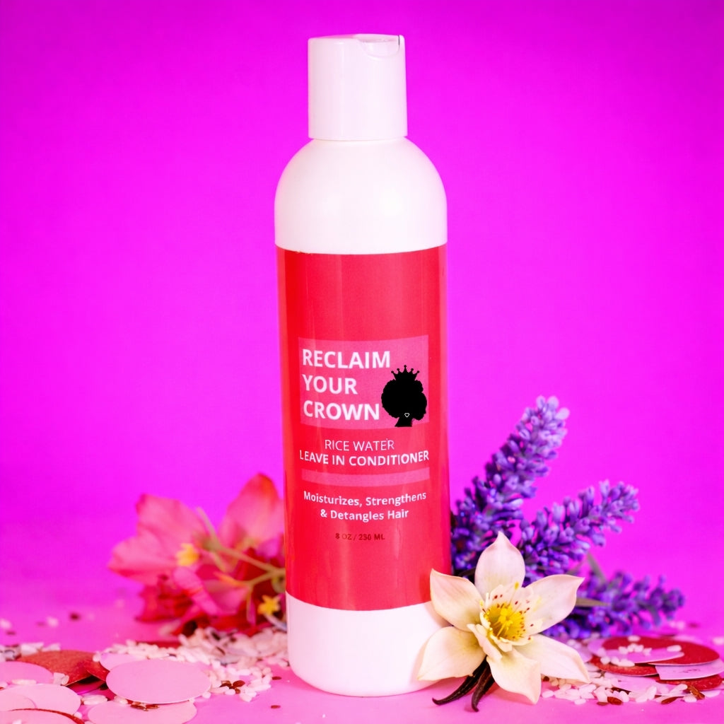 Bottle of 'Reclaim Your Crown' rice water leave-in conditioner on a pink background with flowers.